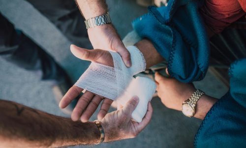 Close-up of two people bandaging an injured hand outdoors, focusing on first aid care.